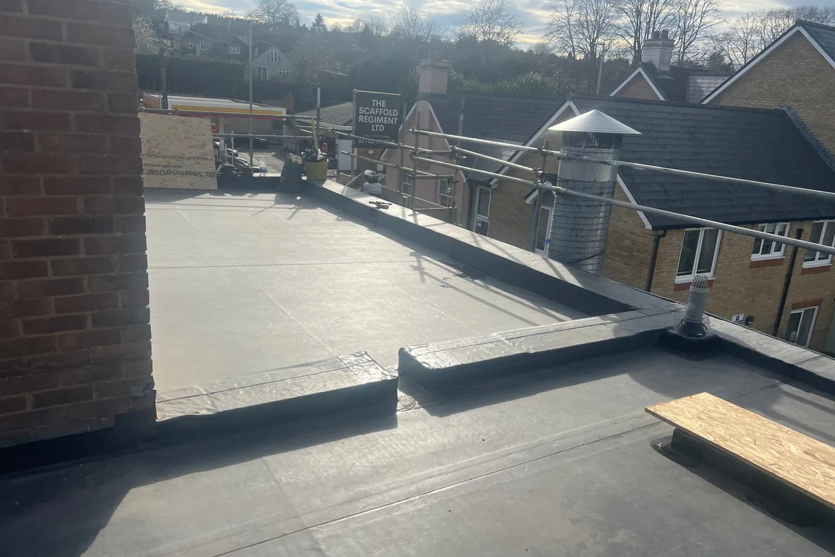 New grey fibreglass flat roof between a brick parapet wall and a pitched roof